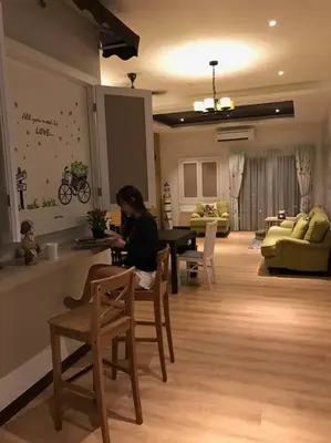 a woman sitting at a table in a living room at Pearl Rice Garden \uff08cottage style\uff09\u7c73\u6a02\u574a\u9802\u5c64\u7530\u56ed\u5f0f\u9ad8\u7ea7\u516c\u5bd3 in Sekincan
