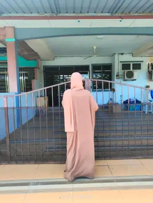 a person in a pink hijab standing in front of a fence at Rumah Singgah in Pantai Remis