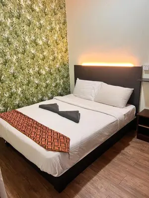a bedroom with a bed with white sheets and a wall at Hotel Citra in Brinchang