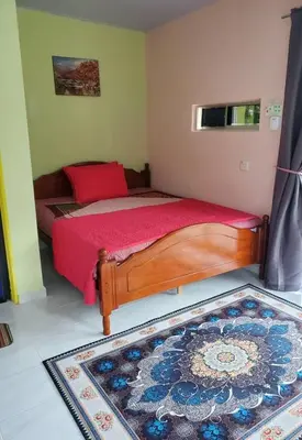 a bedroom with a bed with red sheets and a rug at Inap Desa 3 in Kampong Siput