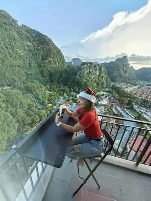 a woman sitting in a chair taking a picture of a mountain at Cozy Suite with 270 Degree Mountain and Theme Park Views in Ipoh