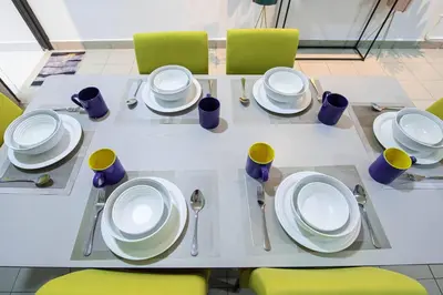 a dining table with white plates and yellow chairs at De Luma (The Rumah)@3bedroom (Sunflower) in Bukit Mertajam